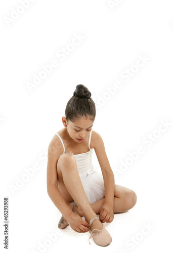 pretty young ballerina student tying up her dance shoes on white