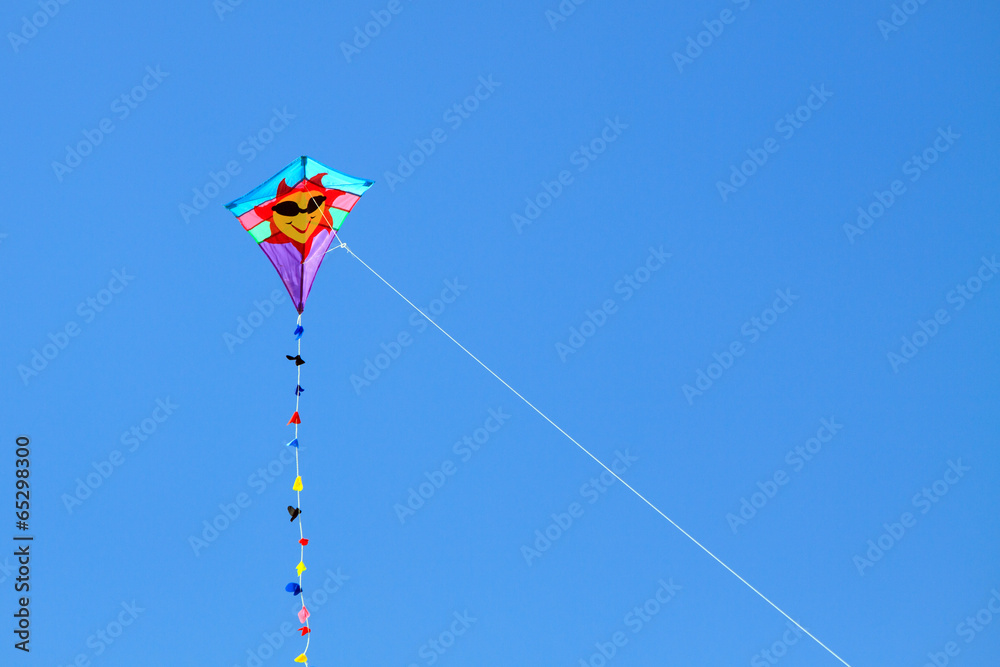 Color DSLR image of smiling face sun kite, flying against a clear, blue sky; horizontal with copy space for text