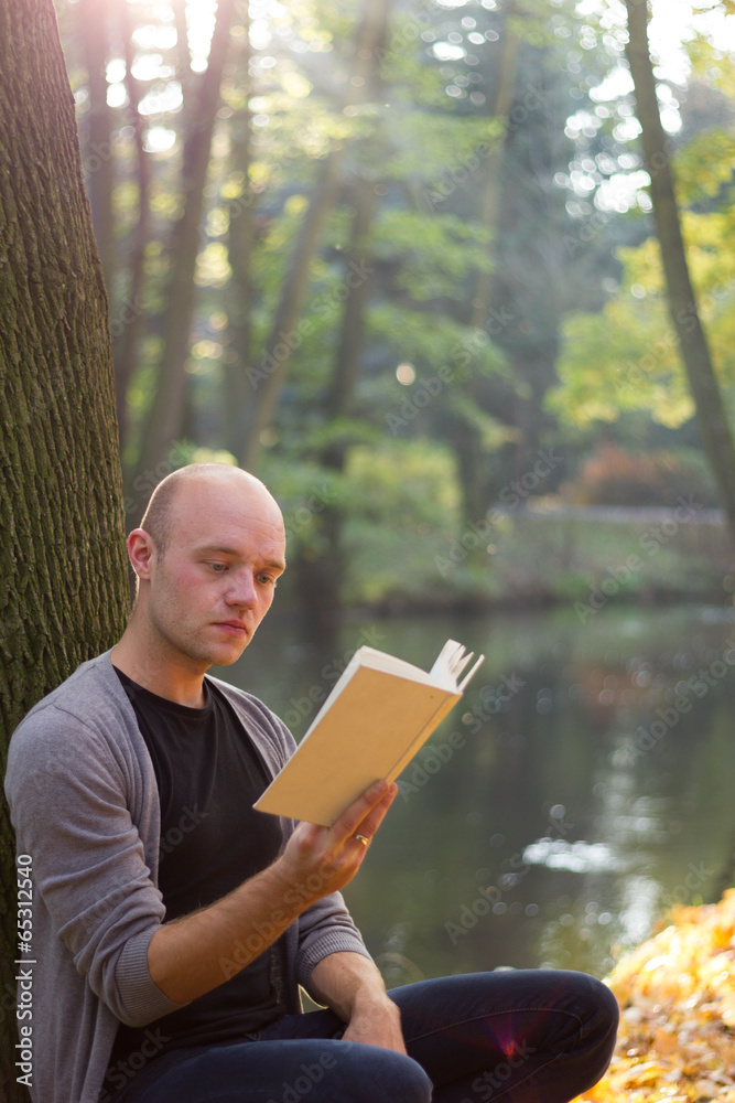 Fototapeta premium Young man relaxing in a park, reading a book