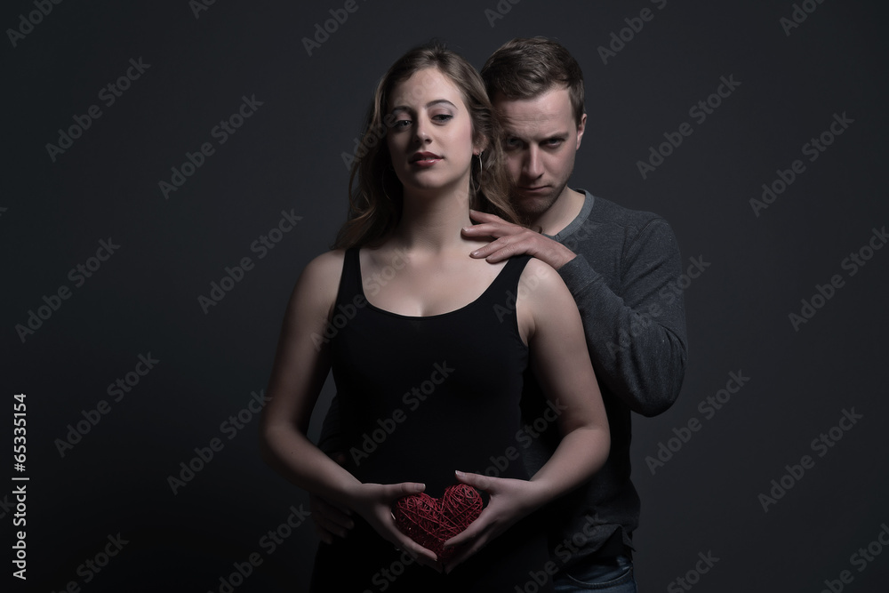 Obraz premium Mysterious fashion couple. She is holding a red heart shape. You