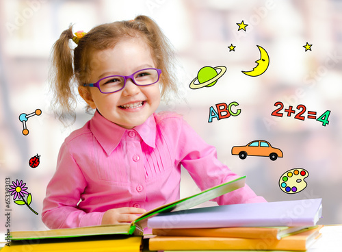 Happy child girl in glasses reading books in library