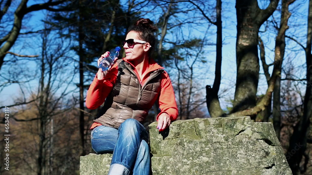 woman drinking mineral water and sitting on the rock in the moun woman drinking mineral water and sitting on the rock in the moun