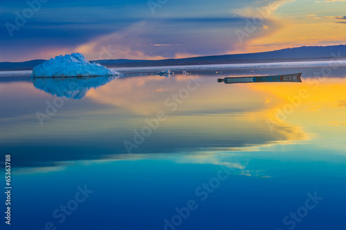 An old boat on the background of iceberg on lake in sunset.