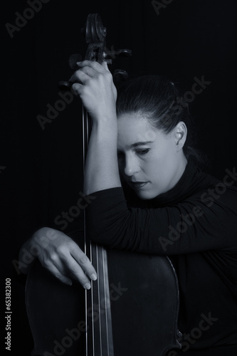 Beautiful brunette holding cello with selective light in red dre