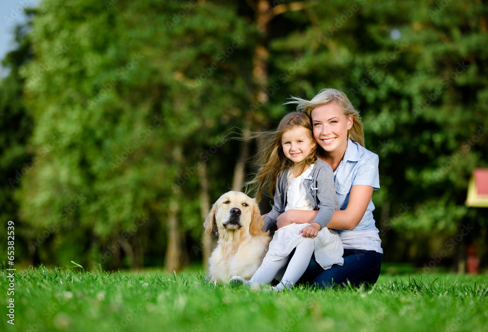 Mother with daughter and labrador sitting on the green grass 