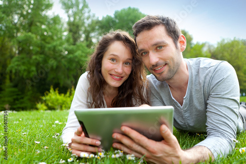 Young beautiful couple using tablet at the park