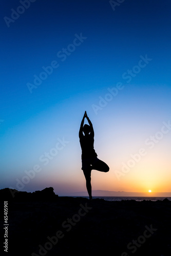 Woman doing yoga tree pose sunset silhouette