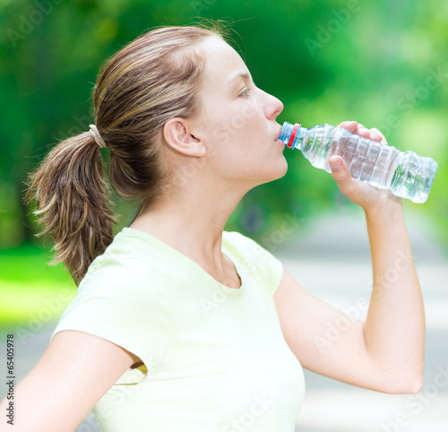 Woman drinking cold mineral water from a bottle after fitness ex