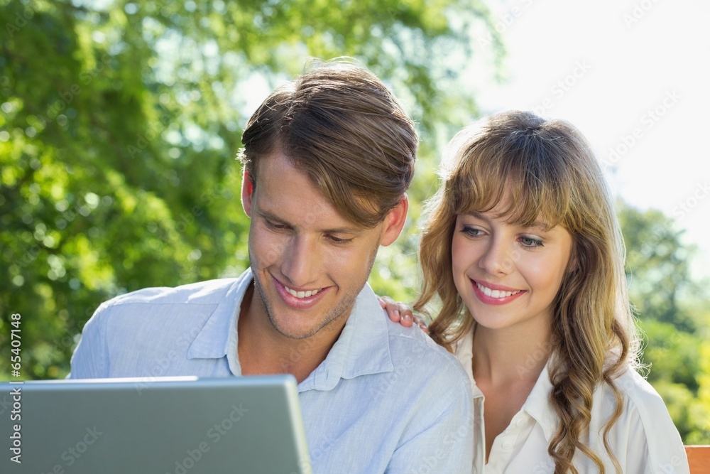 Cute couple sitting on park bench together looking at laptop Cute couple sitting on park bench together looking at laptop
