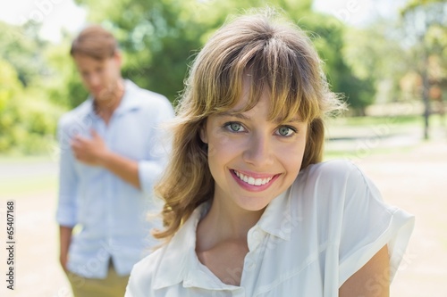 Beautiful blonde smiling at camera with boyfriend in background © WavebreakmediaMicro
