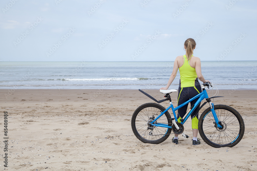 Girl in a green jumpsuit with a blue bicycle on the beach