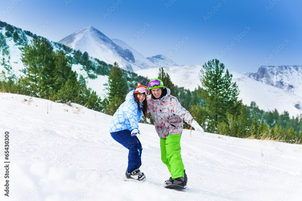 Two friends standing on snowboards balancing