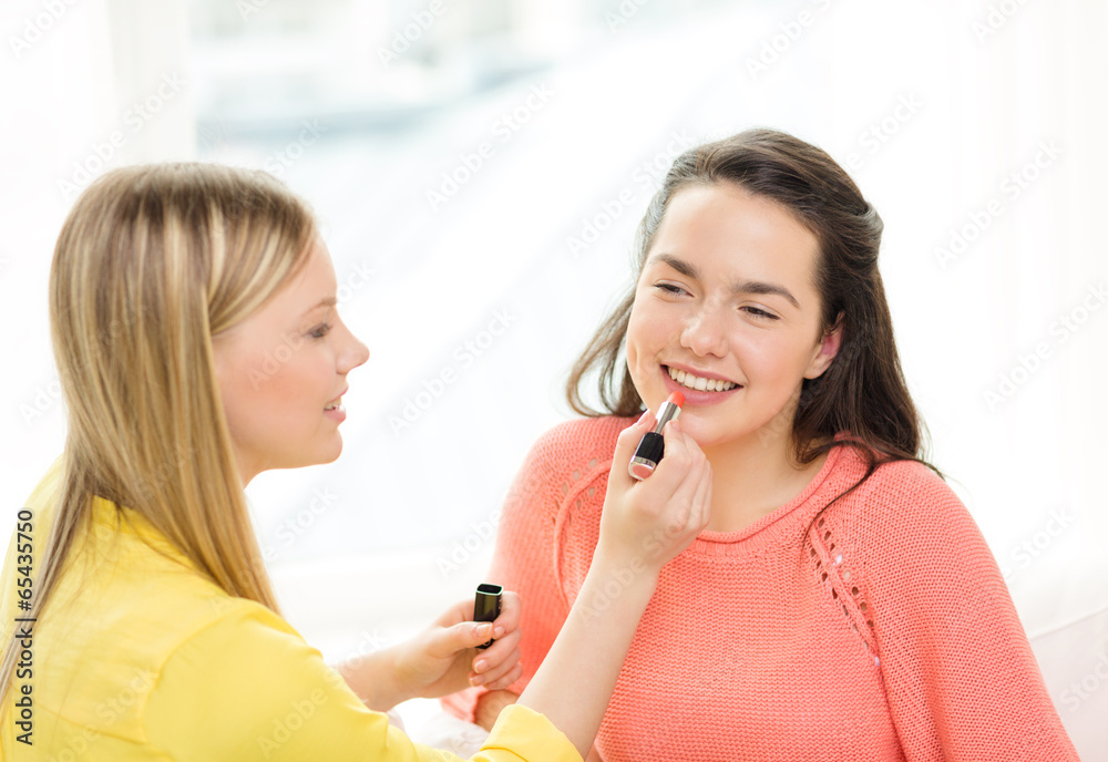 two smiling teenage girls applying make up at home