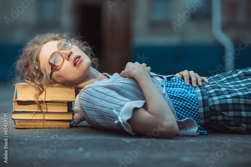 Funny crazy girl student with glasses lying on a pile of books