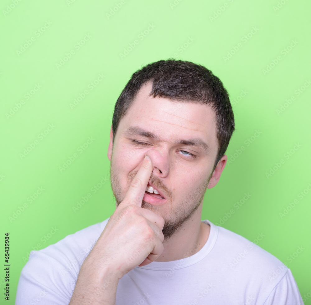 Portrait of a young man with his finger in his nose against gree Portrait of a young man with his finger in his nose against gree