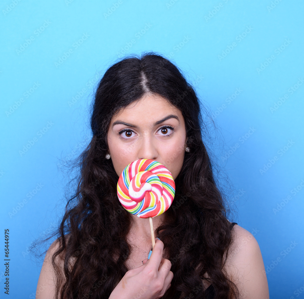 Portrait of woman licking lollipop against blue background