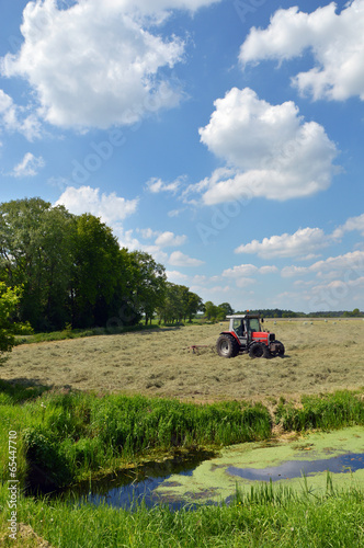 A farm tractor pulling a hay rake in a field