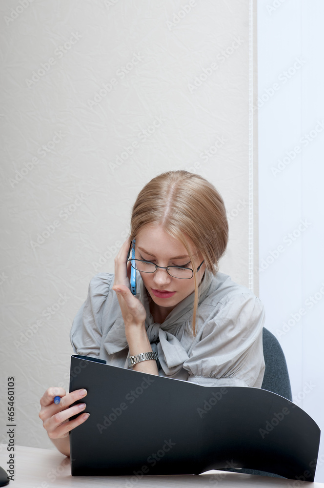 Busy office girl talking on mobile phone and looking at black fo Busy office girl talking on mobile phone and looking at black fo