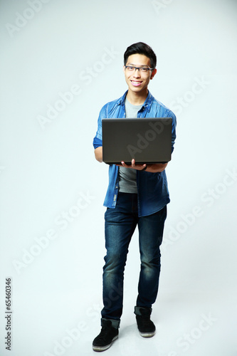 asian man standing with laptop on gray background