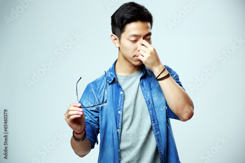 Asian man holding glasses and rubbing his eyes 