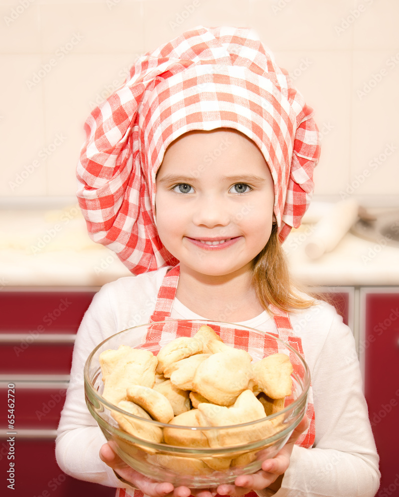 Smiling little girl in chef hat holding bowl with cookies Smiling little girl in chef hat holding bowl with cookies