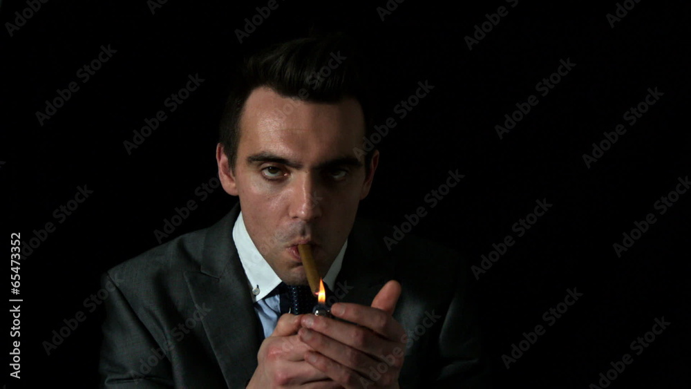 Businessman lighting his cigar on black background Businessman lighting his cigar on black background