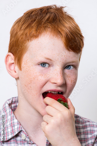 Knabe mit roten Haaren isst eine Erdbeere
