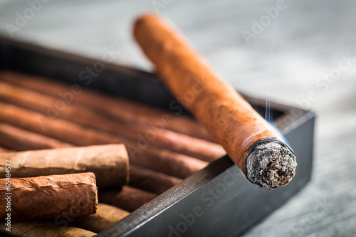 Burning cigar with smoke on wooden humidor photo