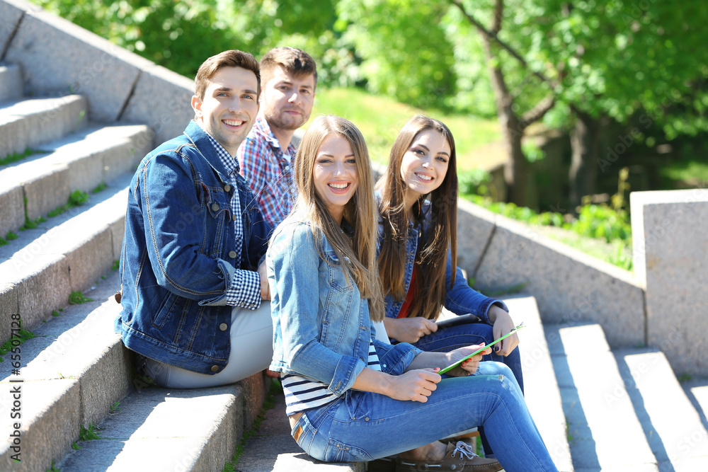Fototapeta premium Happy students sitting on stairs in park