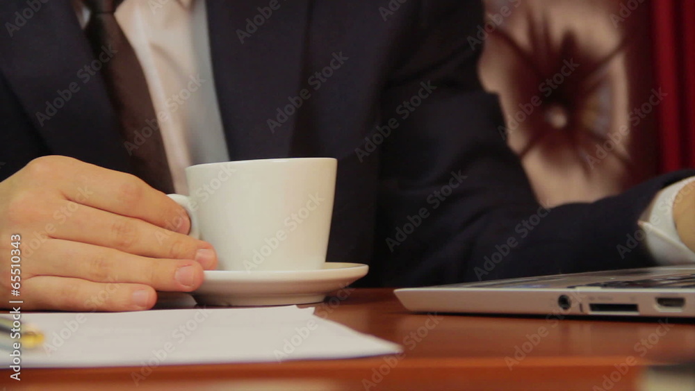 Office worker drinking coffee, checking information on laptop Office worker drinking coffee, checking information on laptop