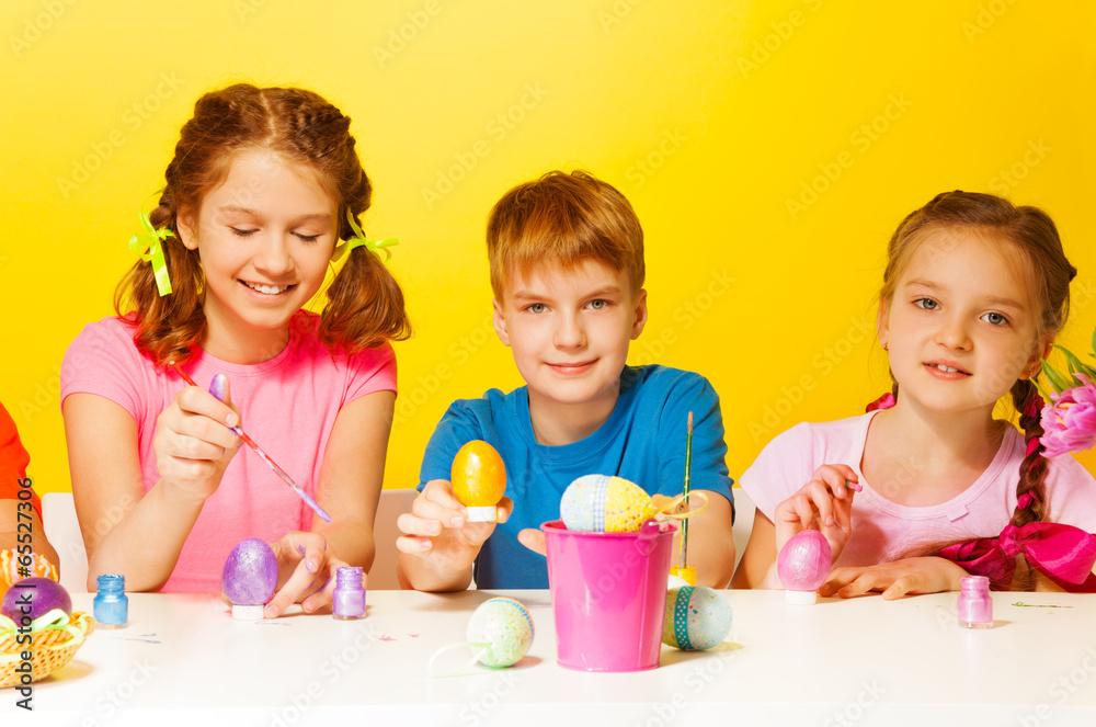 Boy and 2 girls painting Easter eggs at the table Boy and 2 girls painting Easter eggs at the table