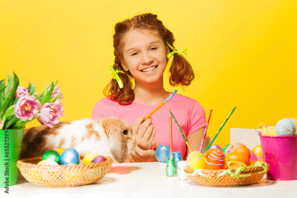 Girl paints Easter eggs with rabbit on the table