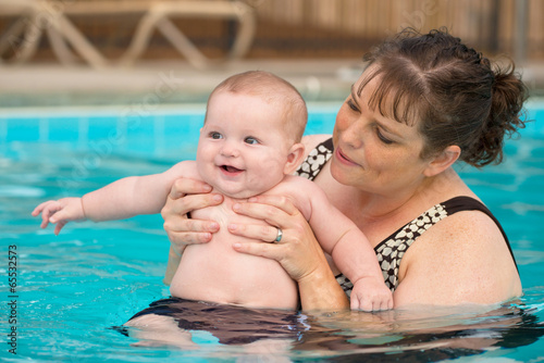 Happy infant baby boy enjoying his first swim in pool