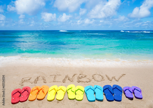 Sign "Rainbow" and color flip flops on sandy beach