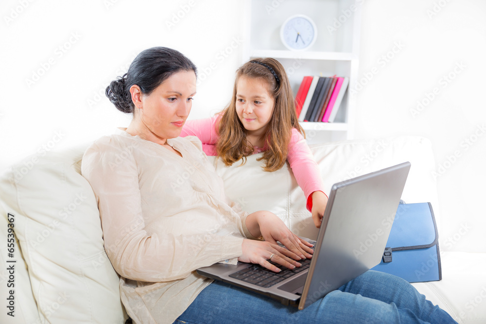 Mother and daughter using laptop together on sofa at home
