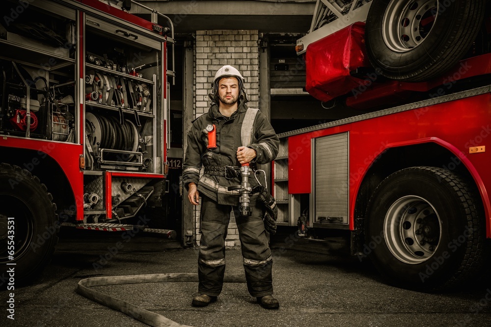 Fototapeta premium Firefighter near truck with equipment with water hose