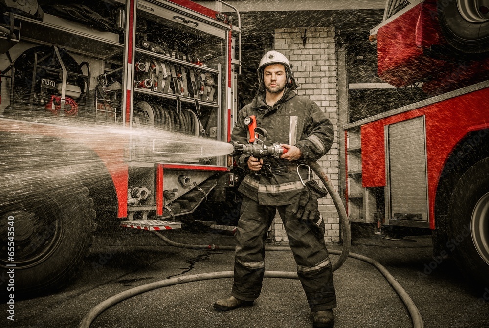 Fototapeta premium Firefighter holding water hose near truck with equipment