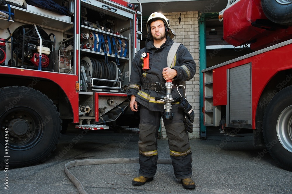 Obraz premium Firefighter near truck with equipment with water hose