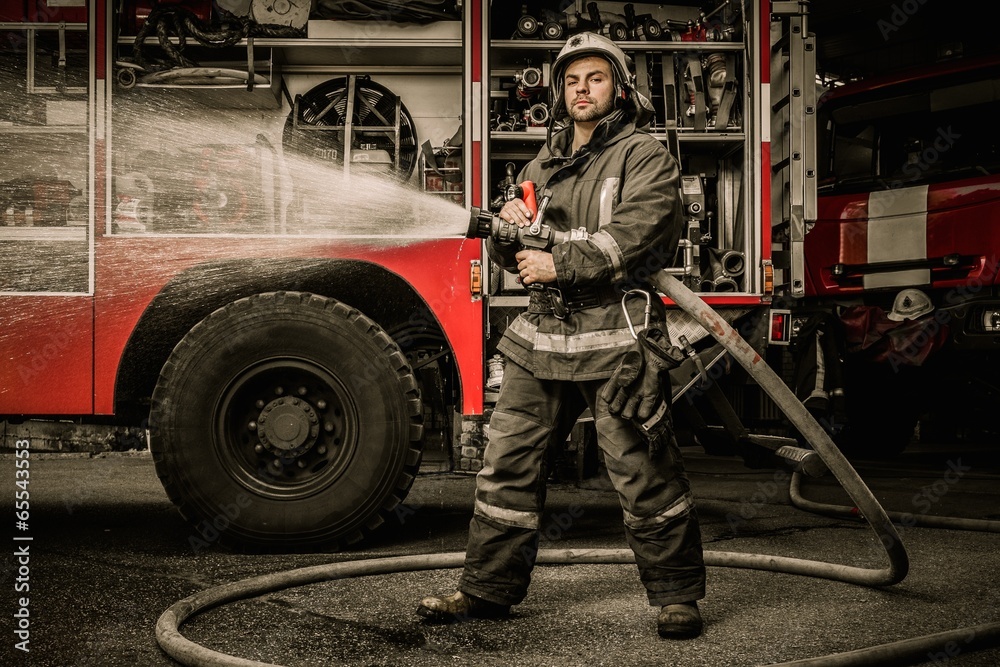 Fototapeta premium Firefighter holding water hose near truck with equipment