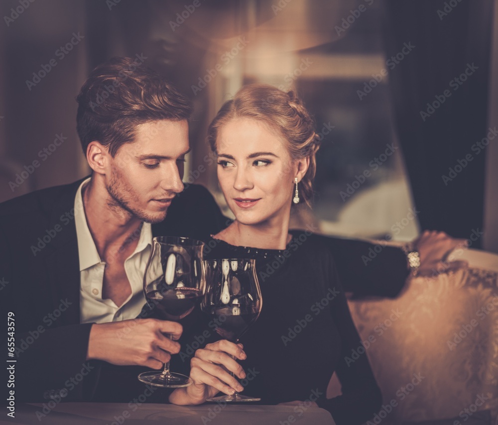 Beautiful young couple with glasses of wine in luxury interior