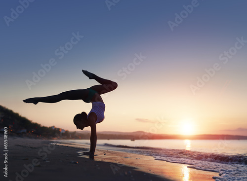 A woman doing a yoga handstand at the beach during a sunrise