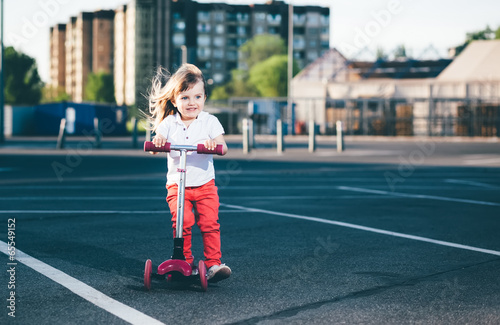 Little beautiful girl riding a scooter