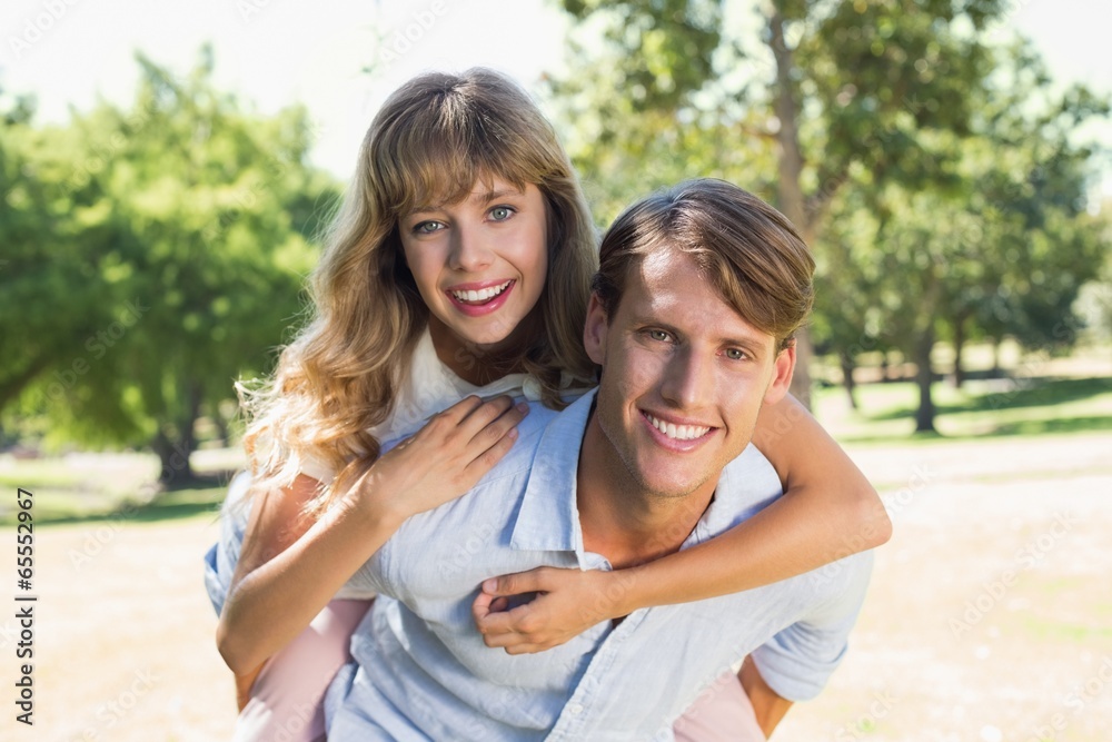 Fototapeta premium Man giving his pretty girlfriend a piggy back in the park smilin