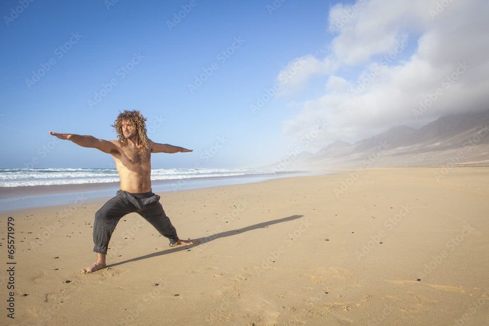 young man doing yoga warrior pose on the beach