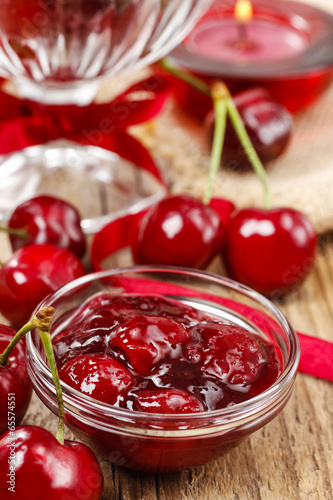 Bowl of cherry jam on wooden table and fresh cherries around