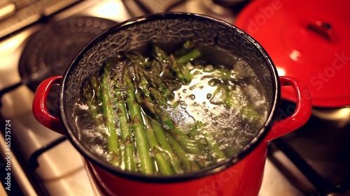 A bunch of asparagus boiling in a red steel bowl full of water