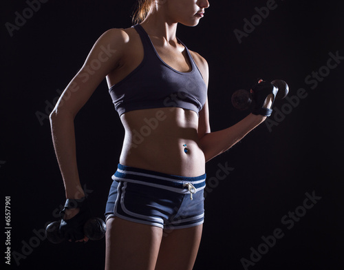 Torso of a young fit woman lifting dumbbells