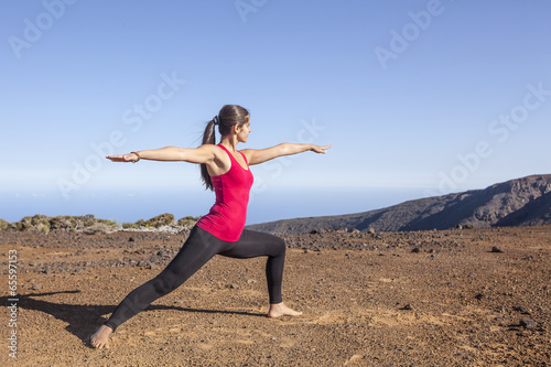 Young woman practicing yoga warrior pose on a desert mountain