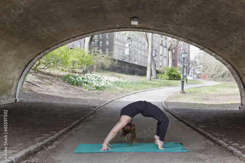 A young woman in Central Park, in a black leotard and leggings, doing yoga.