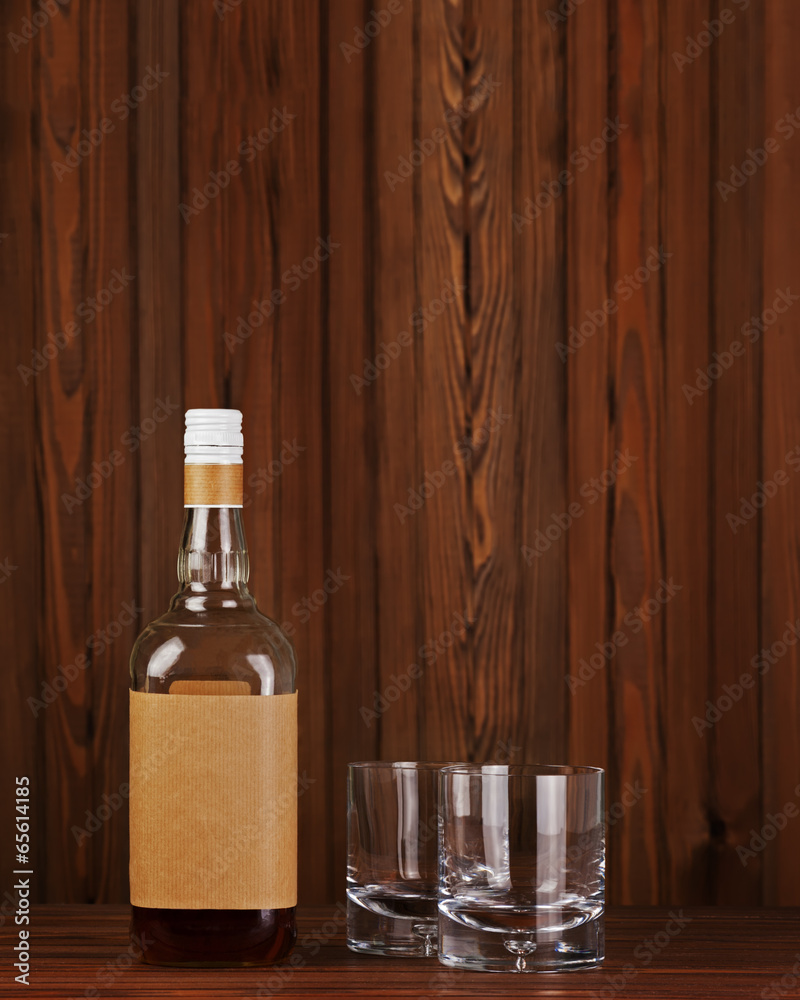 Glasses with ice for whiskey and bottle on wooden background.
